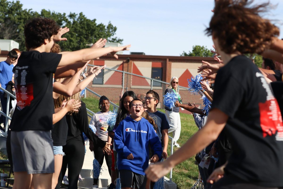 the Oak Street Singers, HOSA, Volleyball, Cross Country, and Football representatives make a tunnel to welcome the Meadowbrook students outside for the first ever Homecoming Traveling Parade.