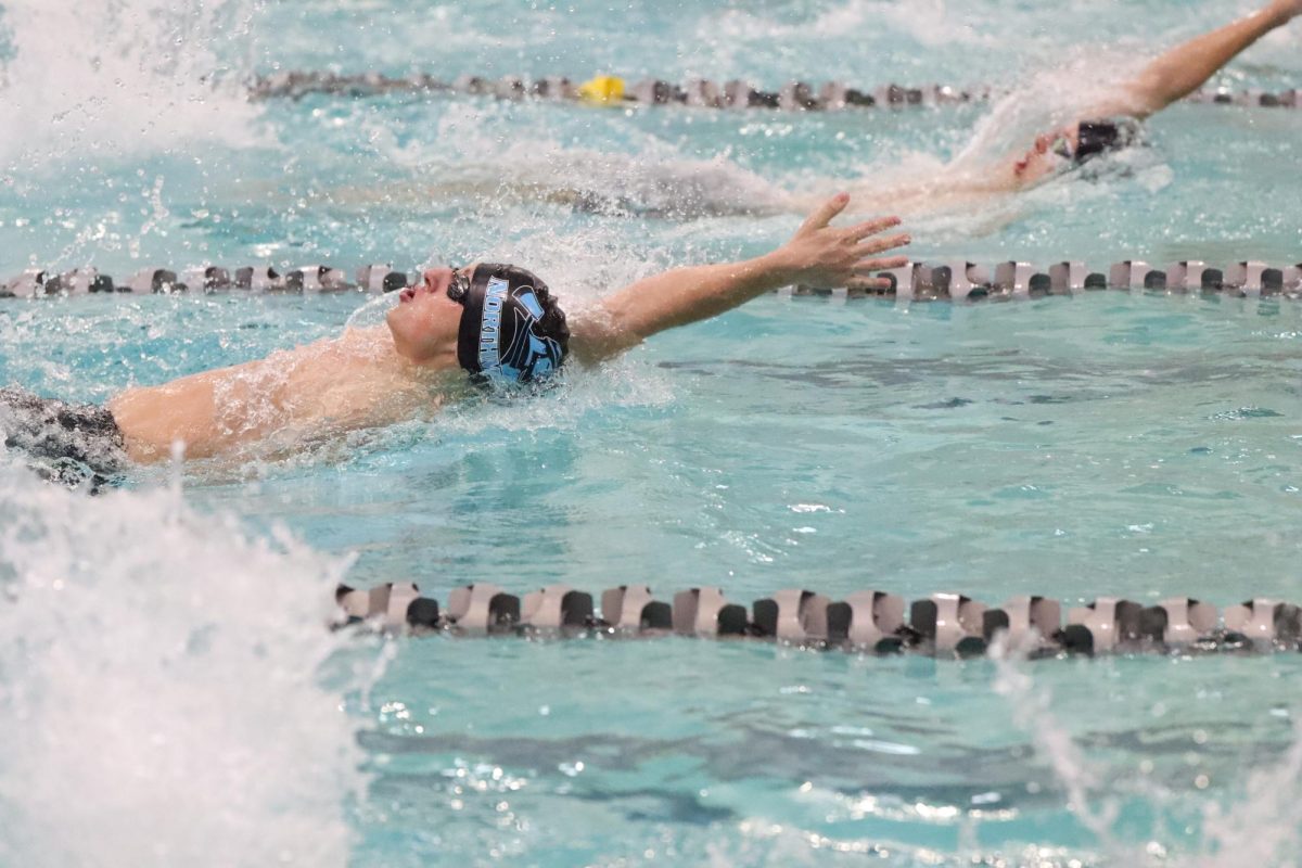 Shooting through the water, one hand breaks into the water as another rises from underneath. Senior Ben Place racing the backstroke at State Swim. He got into State during his conference and has preparing to do cut down time ever since. 